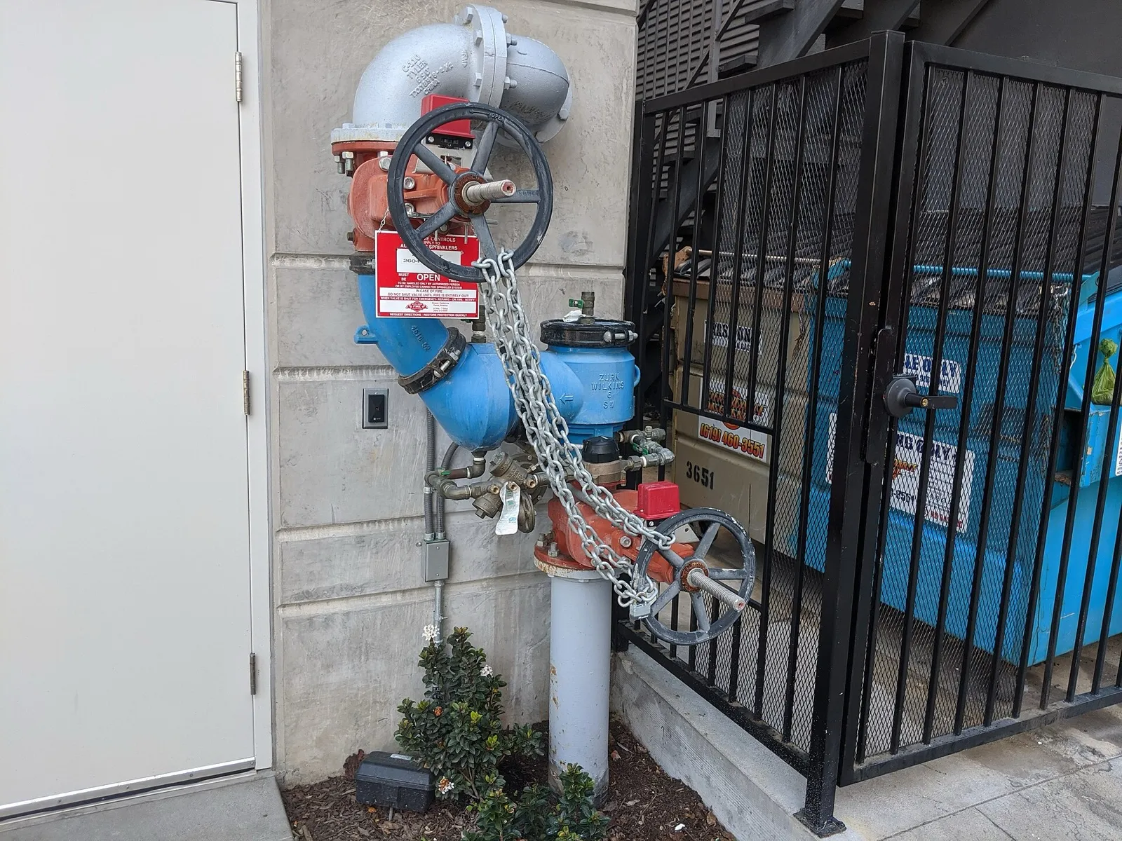 A large vertical fire-line backflow preventer outside a commercial building